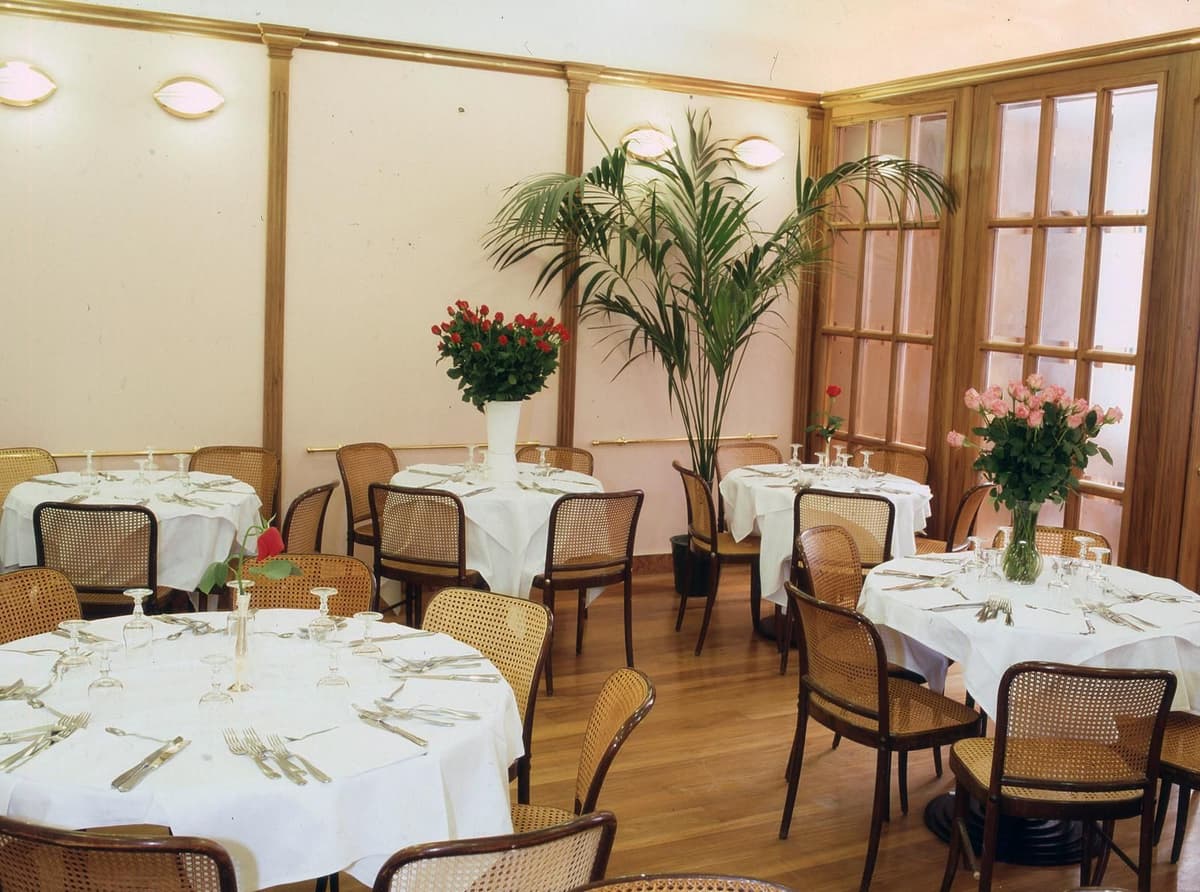 Spacious restaurant dining area with round tables, wicker chairs, and floral centerpieces for group dining.