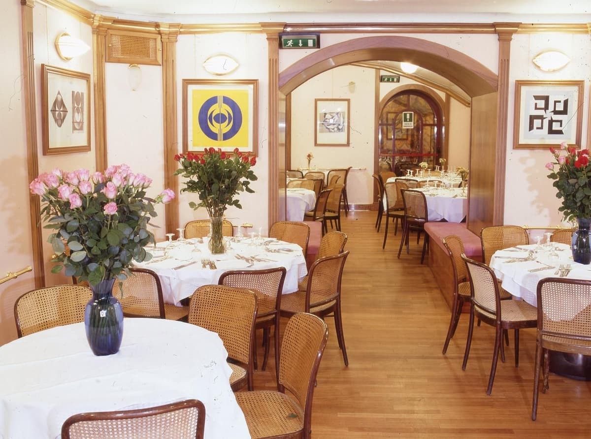 Connected restaurant dining rooms with elegant décor, white table settings, and warm lighting.